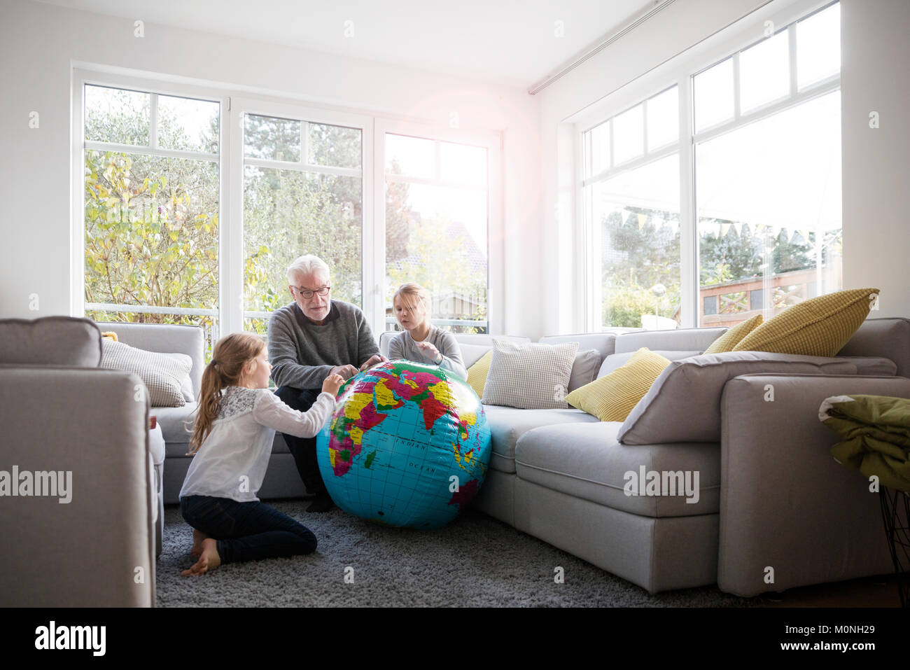 Zwei Mädchen und Großvater mit Globus im Wohnzimmer Stockfoto