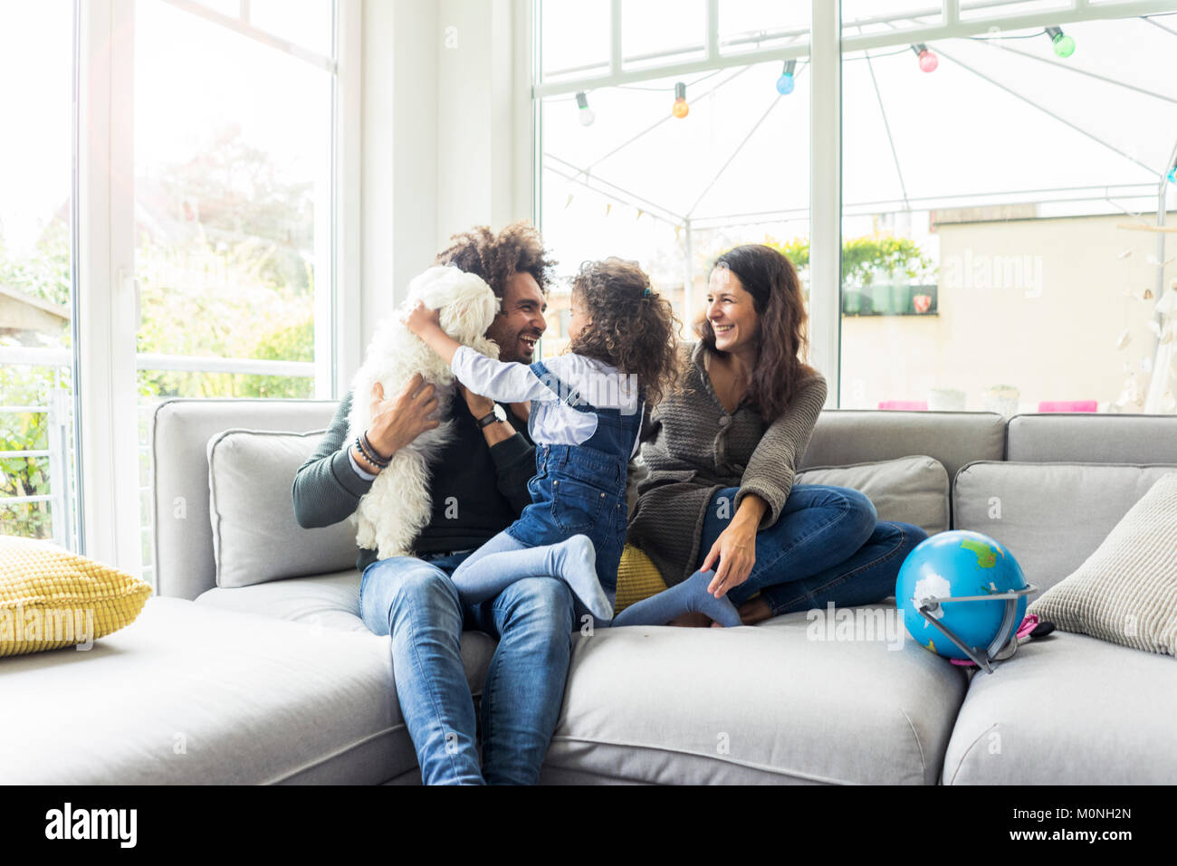 Glückliche Familie mit Hund sitzen zusammen im gemütlichen Wohnzimmer Stockfoto
