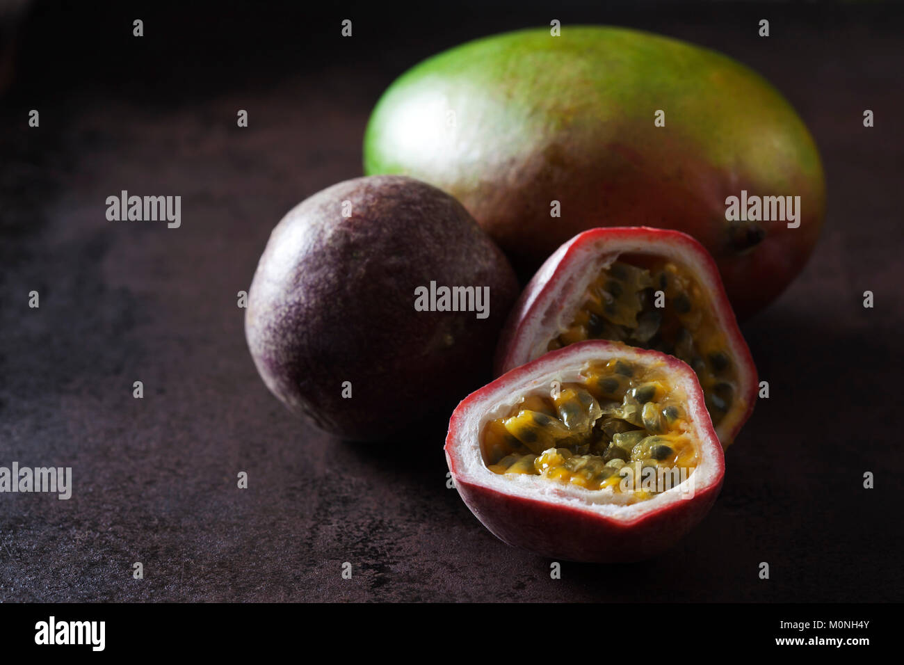 Ganze und aufgeschnittene Passionsfrucht und Mango, auf dunklem Boden Stockfoto