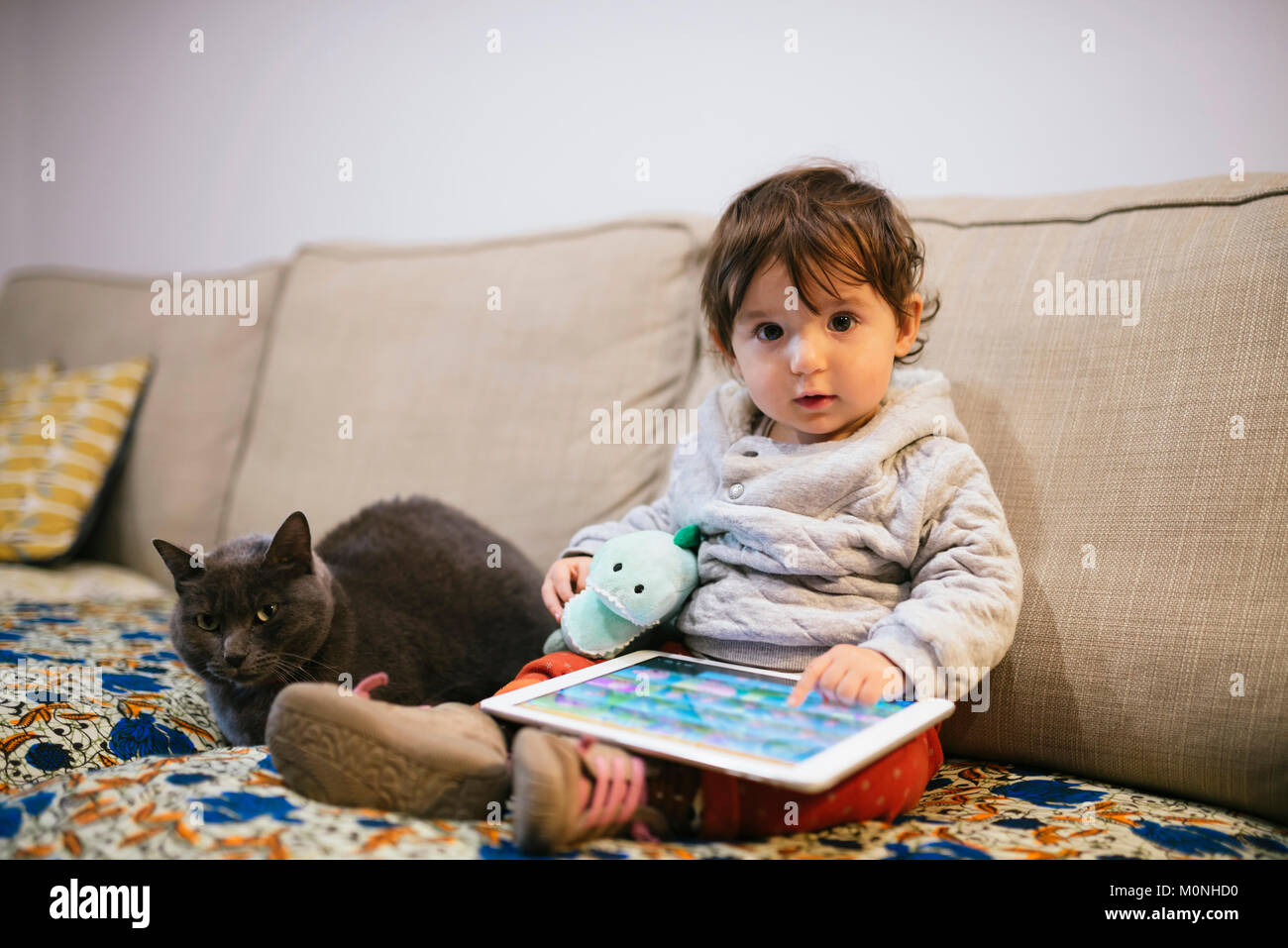 Baby Mädchen sitzen auf der Couch Videos auf einem Tablett mit einer Katze Stockfoto