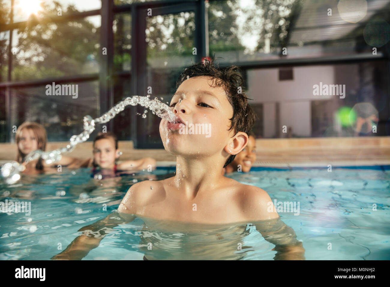 Junge mit Freunden im Hallenbad spucken Wasser Stockfoto