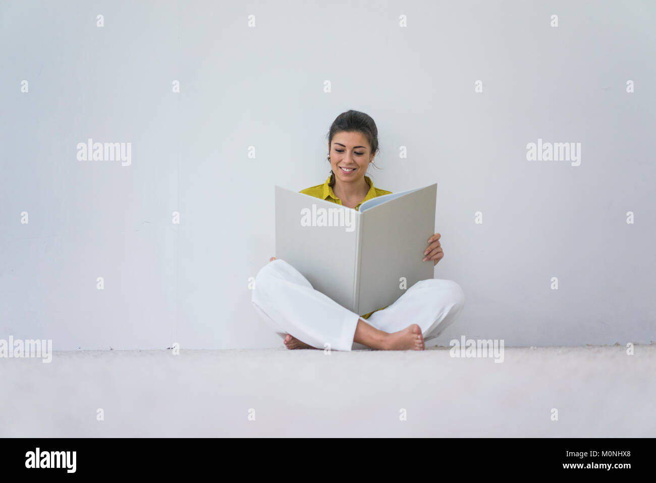Lächelnde Frau sitzen auf dem Boden lesen übergroßen Buch Stockfoto