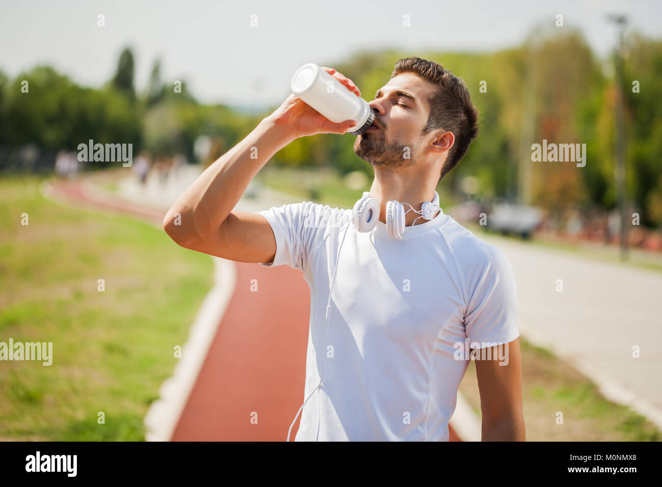 Junge Mann ist Trinkwasser nach dem Joggen an einem sonnigen Tag. Stockfoto