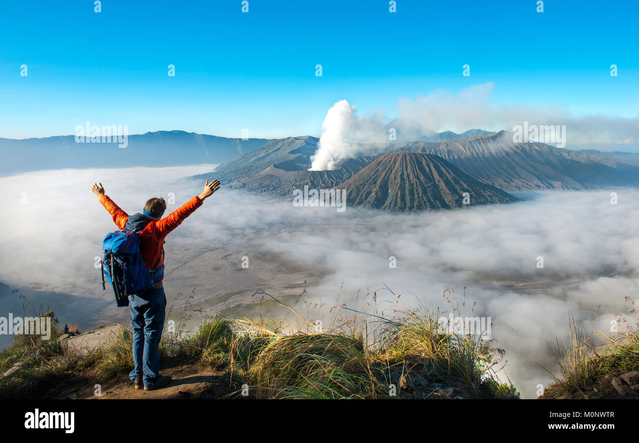 Junger Mann mit erhobenen Armen vor der vulkanischen Landschaft, Blick in Tengger Caldera, Rauchender Vulkan Gunung Bromo, vor Mt. Stockfoto
