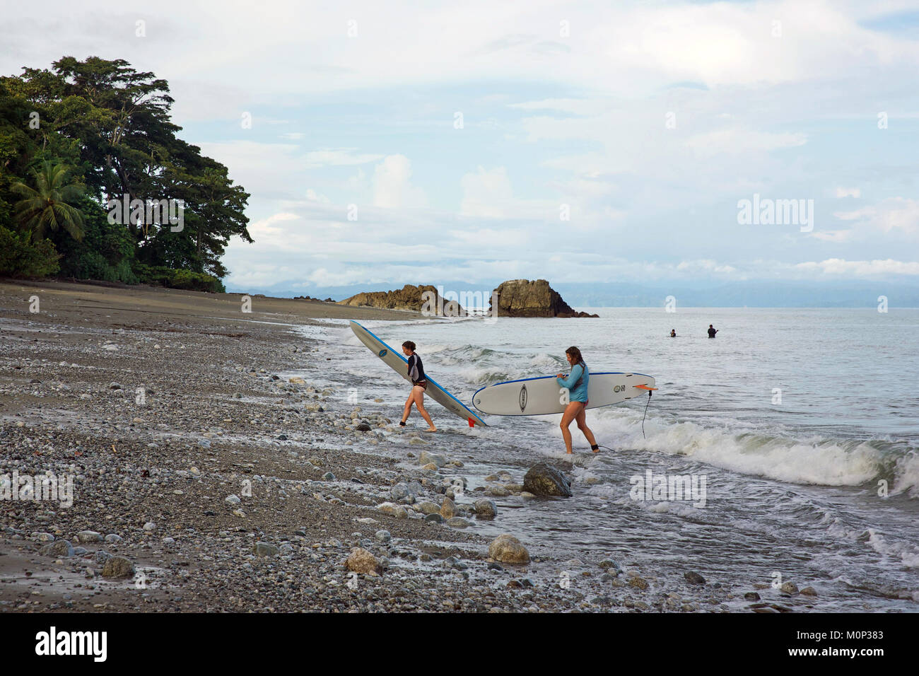Costa Rica, Halbinsel Osa, zwei junge Surfer aus dem Ozean auf einem Kieselstrand mit dem primären Wald gesäumt Stockfoto