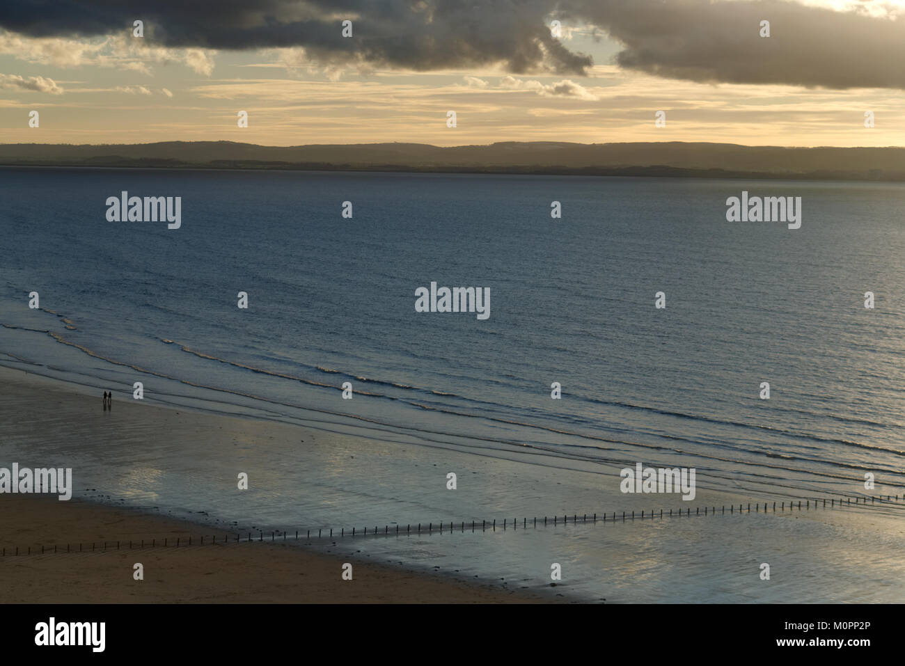 Blick auf Brean Strand mit Silhouette von Wellen brechen Beiträge und Menschen zu Fuß entlang der Küste Stockfoto