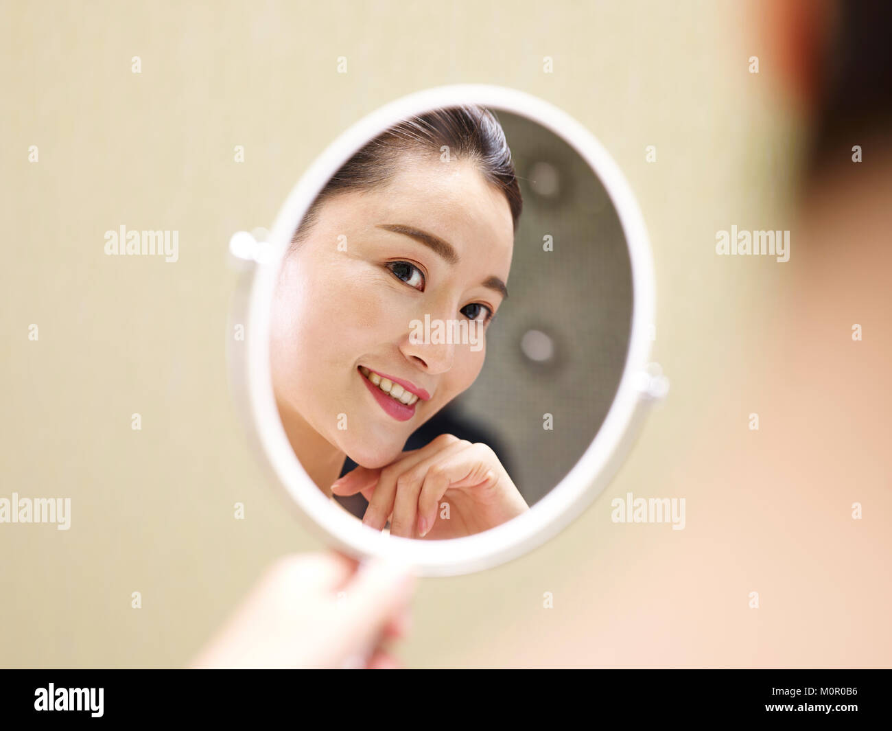 Schöne junge asiatische Frau an sich selbst im Spiegel zu betrachten, glücklich und lächelnd. Stockfoto