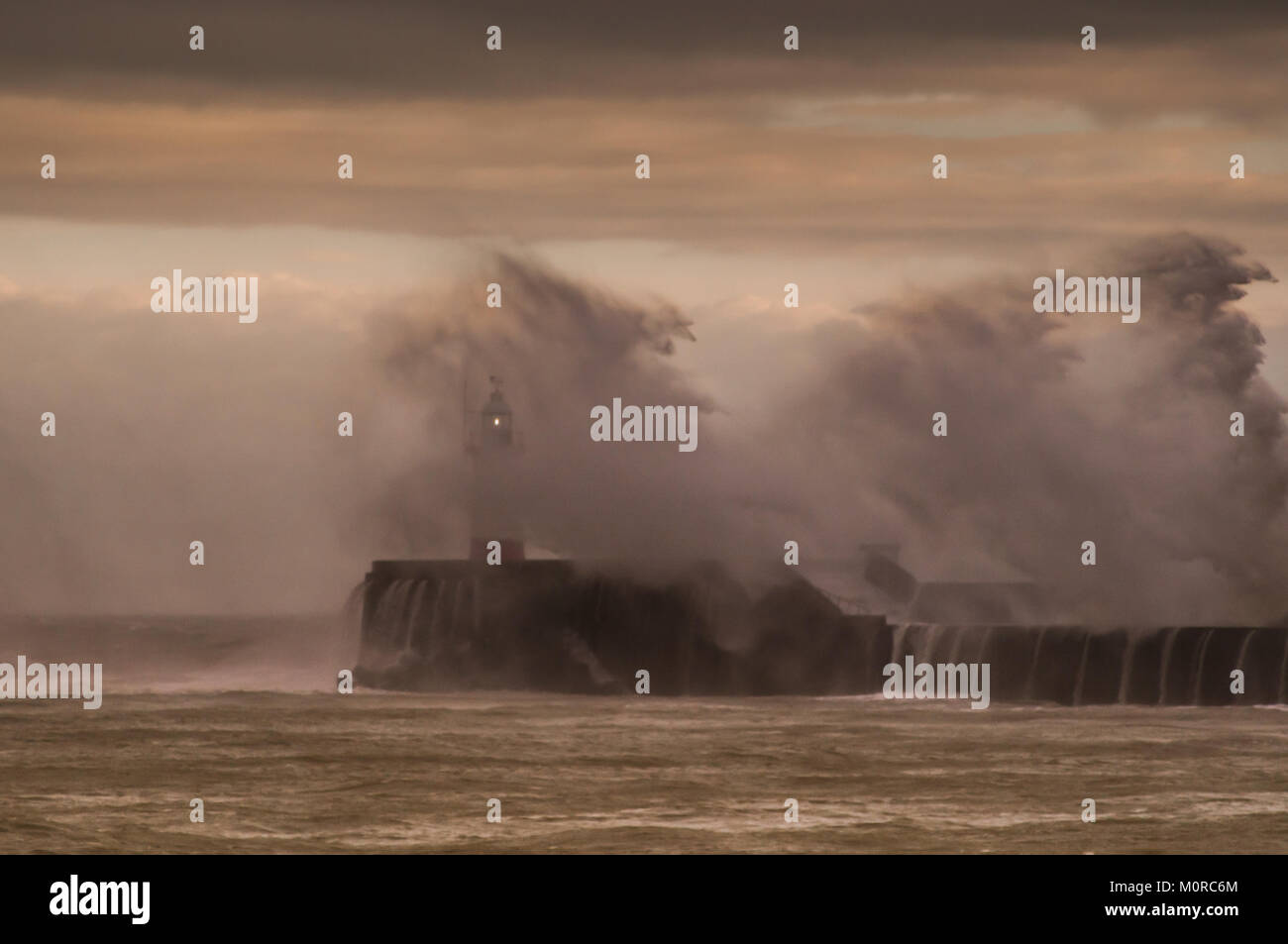 Newhaven, East Sussex, Großbritannien. Januar 2018. Wetter in Großbritannien. Starker Wind und reißender Regen an der Südküste. Die Wellen schlagen den Westarm und den Leuchtturm in den Pfennig. Sun versuchte, die Wolkendecke zu durchbrechen und dabei glorreiche Farben zu schaffen. Stockfoto