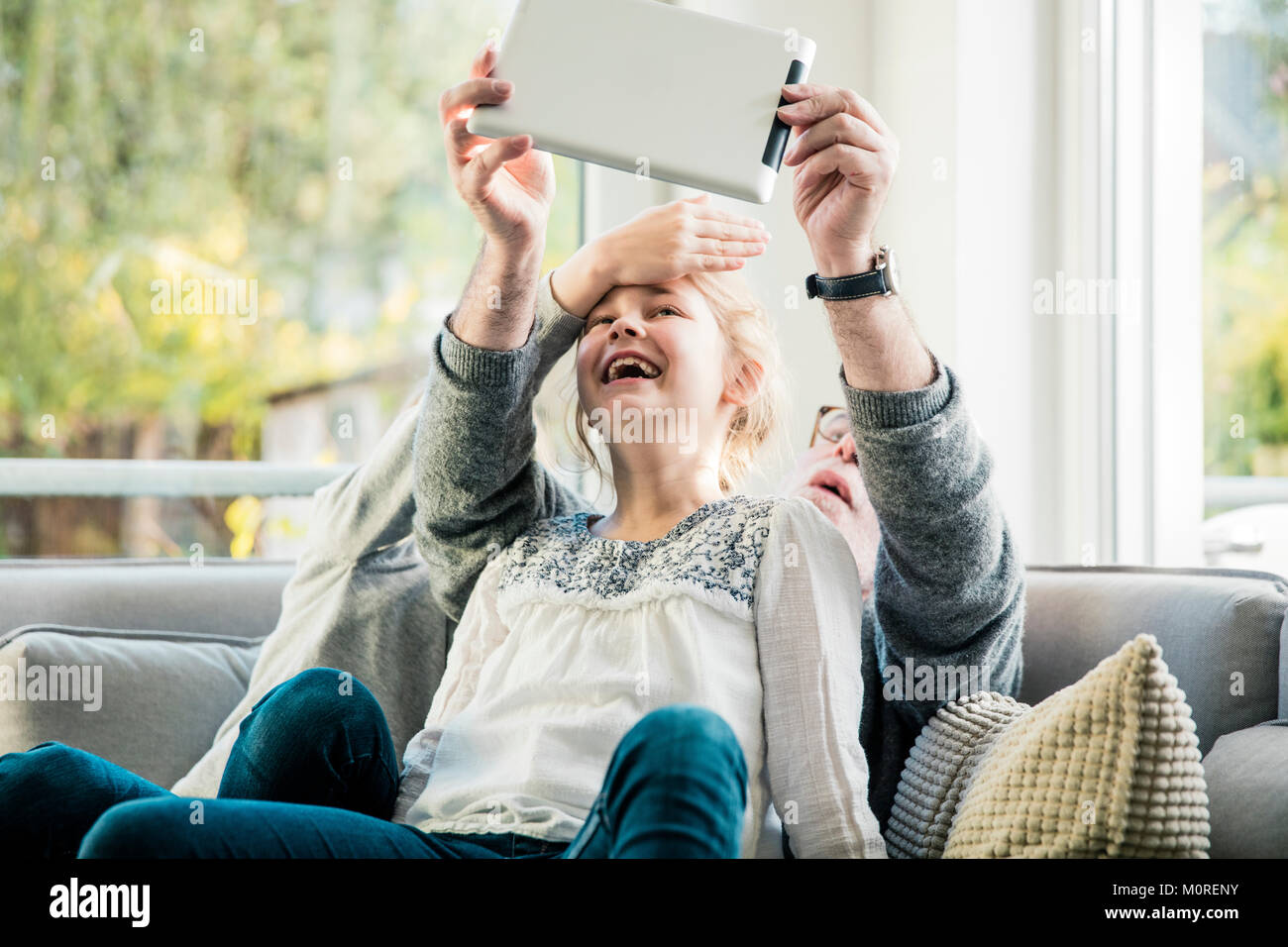 Zwei glückliche Mädchen und Großvater auf dem Sofa ein selfie mit Tablet Stockfoto