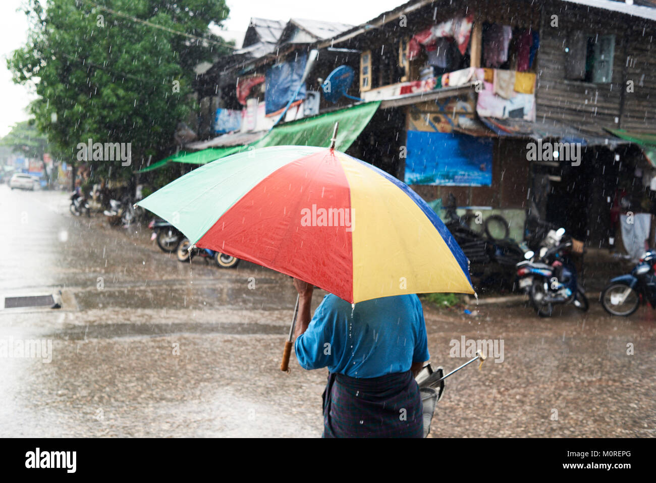 Nicht erkennbare alte asiatische Mann mit einem bunten Regenschirm in der Regenzeit. Stockfoto