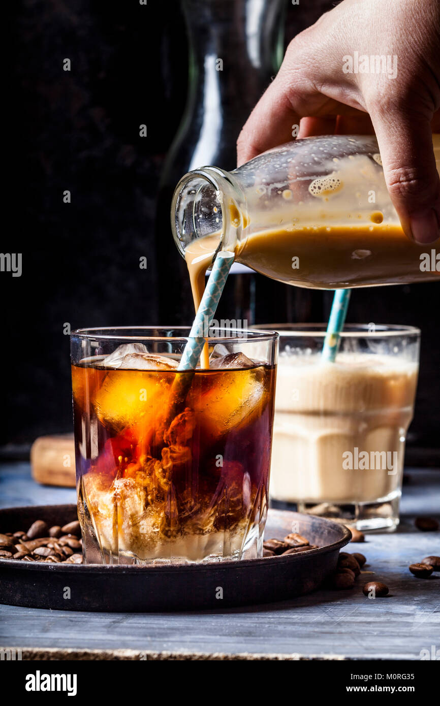 Hand gießen hausgemachte Vanille würzte Kaffeesahne in ein Glas mit Eiskaffee Stockfoto
