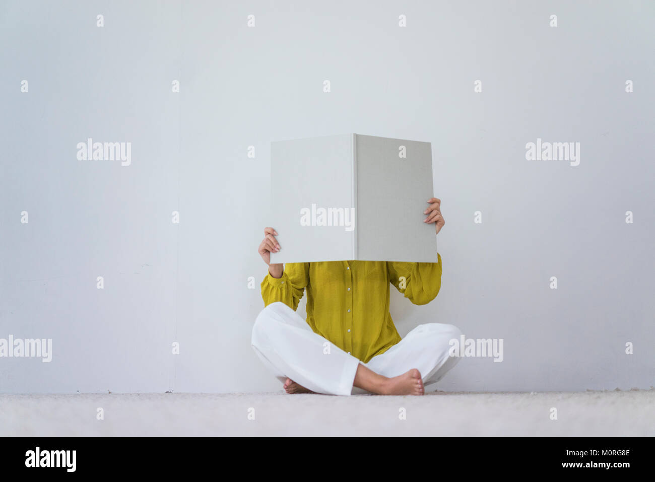 Frau sitzt auf dem Boden ihr Gesicht verstecken sich hinter einem übergroßen Buch Stockfoto