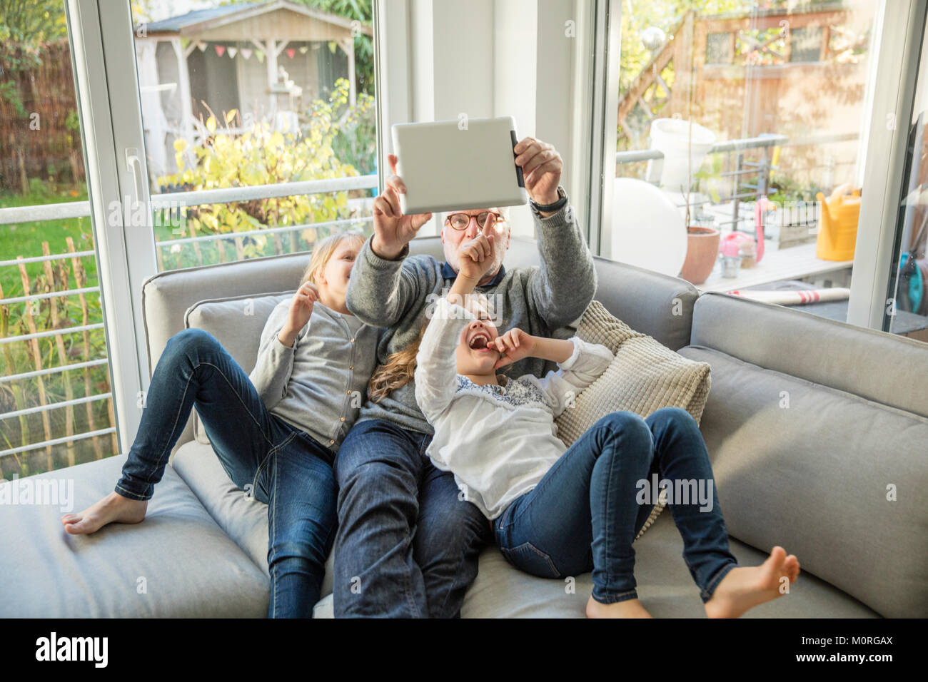 Zwei glückliche Mädchen und Großvater auf dem Sofa ein selfie mit Tablet Stockfoto