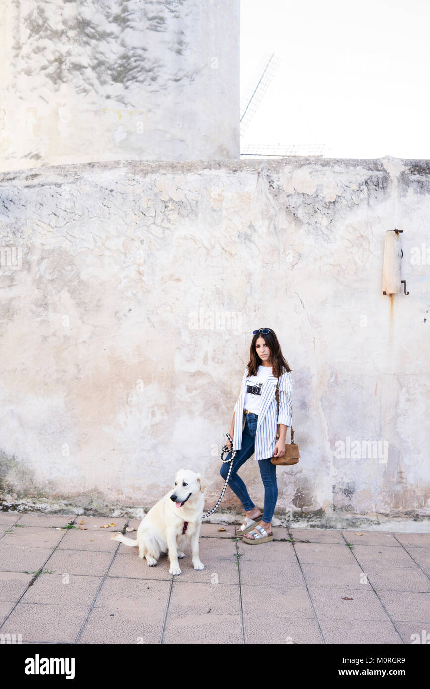Hübsche junge Mädchen mit einem goldenen Hund auf der Straße gegen eine Wand. Stockfoto