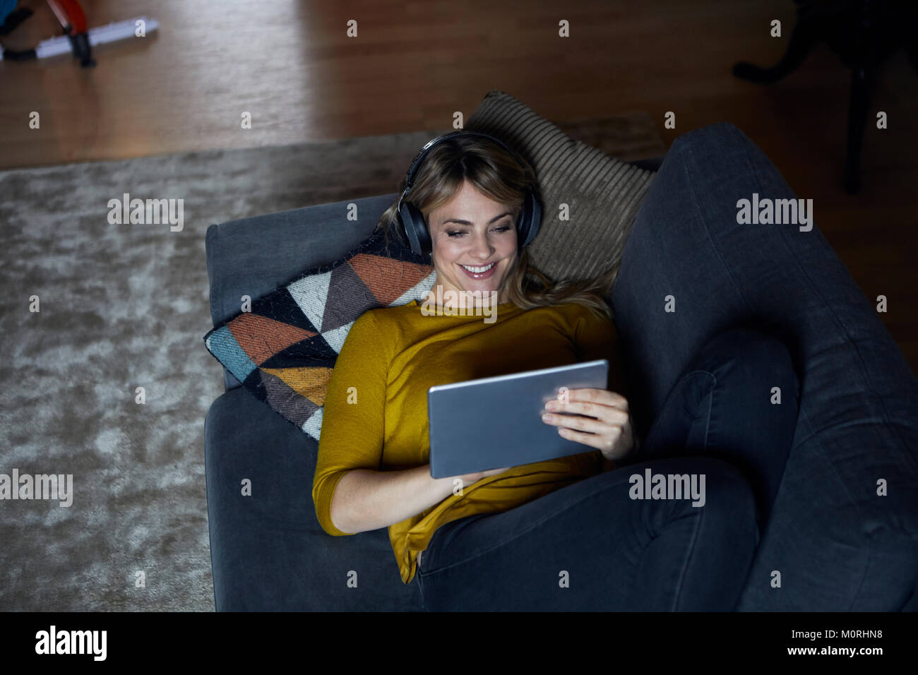 Porträt der lächelnde Frau, die auf die Verwendung von Kopfhörern und Tablet couch Stockfoto
