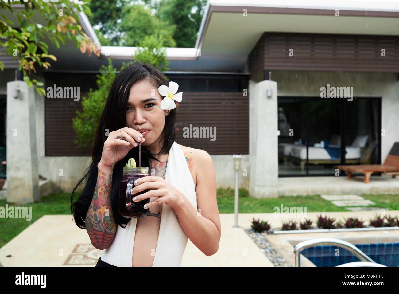 Tätowiert asiatischen brunette Mädchen trinken Sie einen Cocktail und Kamera in einem Sommer Villa. Stockfoto