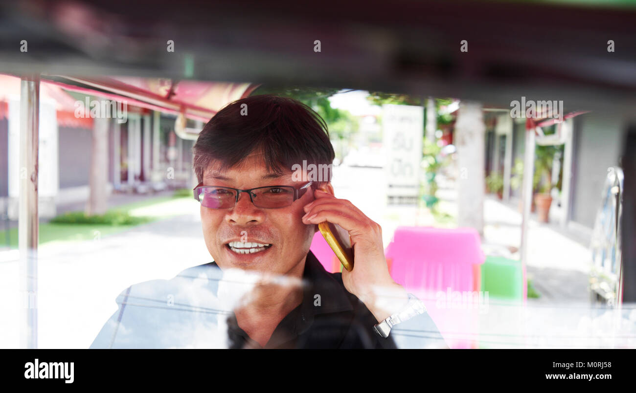 Thai Tuk-Tuk Fahrer sprechen über das Telefon in seinem Fahrzeug auf der Straße in Bangkok, Thailand. Stockfoto