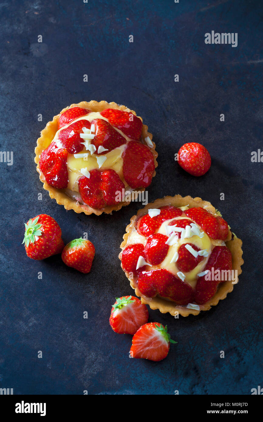 Zwei Erdbeere Törtchen mit Vanillepudding und weiße Schokolade rasieren auf dunklem Boden Stockfoto