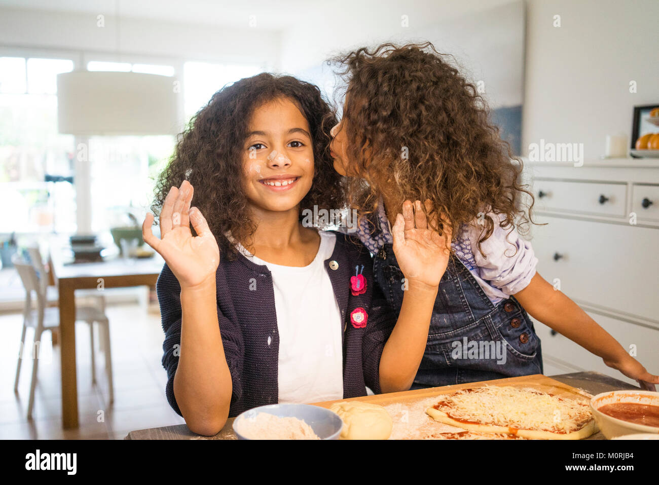 Kleines Mädchen küssen Schwester in Küche, backen Pizza Stockfoto
