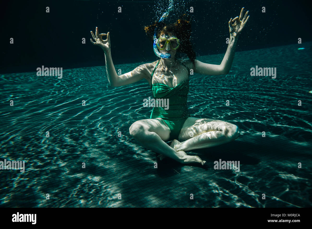 Frau mit Taucherbrille und Schnorchel im Yoga sitting Pose unter Wasser in einem Pool Stockfoto