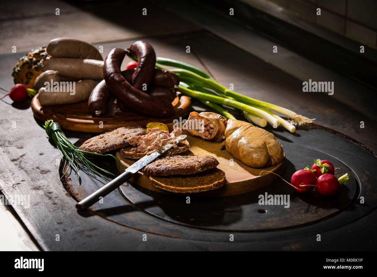 Leberwurst, Blutwurst, Frühlingszwiebeln, rote Rübe, Schnittlauch, Senf, Brot auf Schneidebrett, Heizplatte Stockfoto