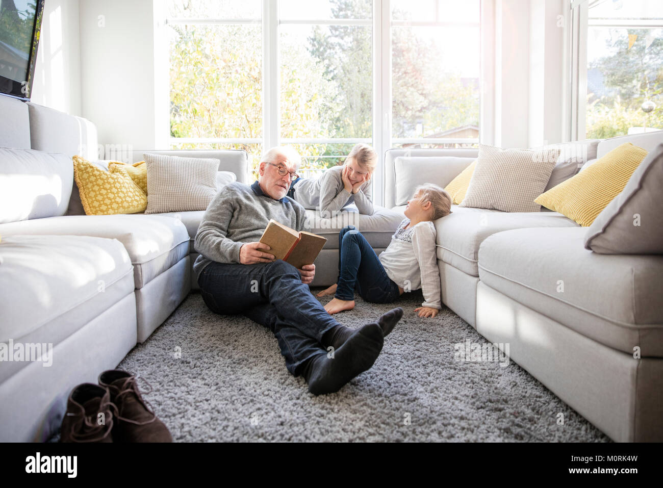Zwei Mädchen und Großvater Lesung buchen Sie im Wohnzimmer Stockfoto
