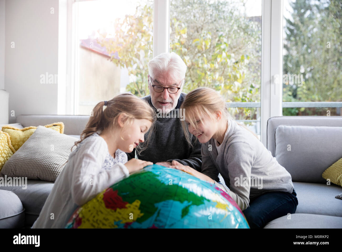Zwei Mädchen und Großvater mit Globus im Wohnzimmer Stockfoto