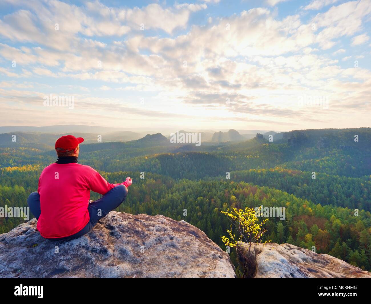 Sitzung Wanderer auf Rock. Mann in Rot Schwarz warme Kleidung sitzt auf Felsen und weiten Blick genießen. Blick in Misty hügeligen Tal unten Stockfoto