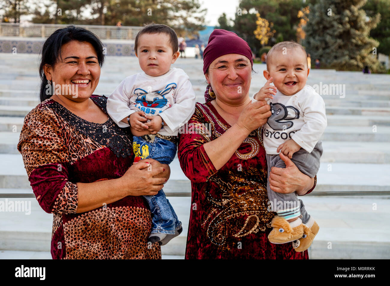 Zwei usbekische Frauen mit Babys für ein Foto posieren Am Registan, Samarkand, Usbekistan Stockfoto