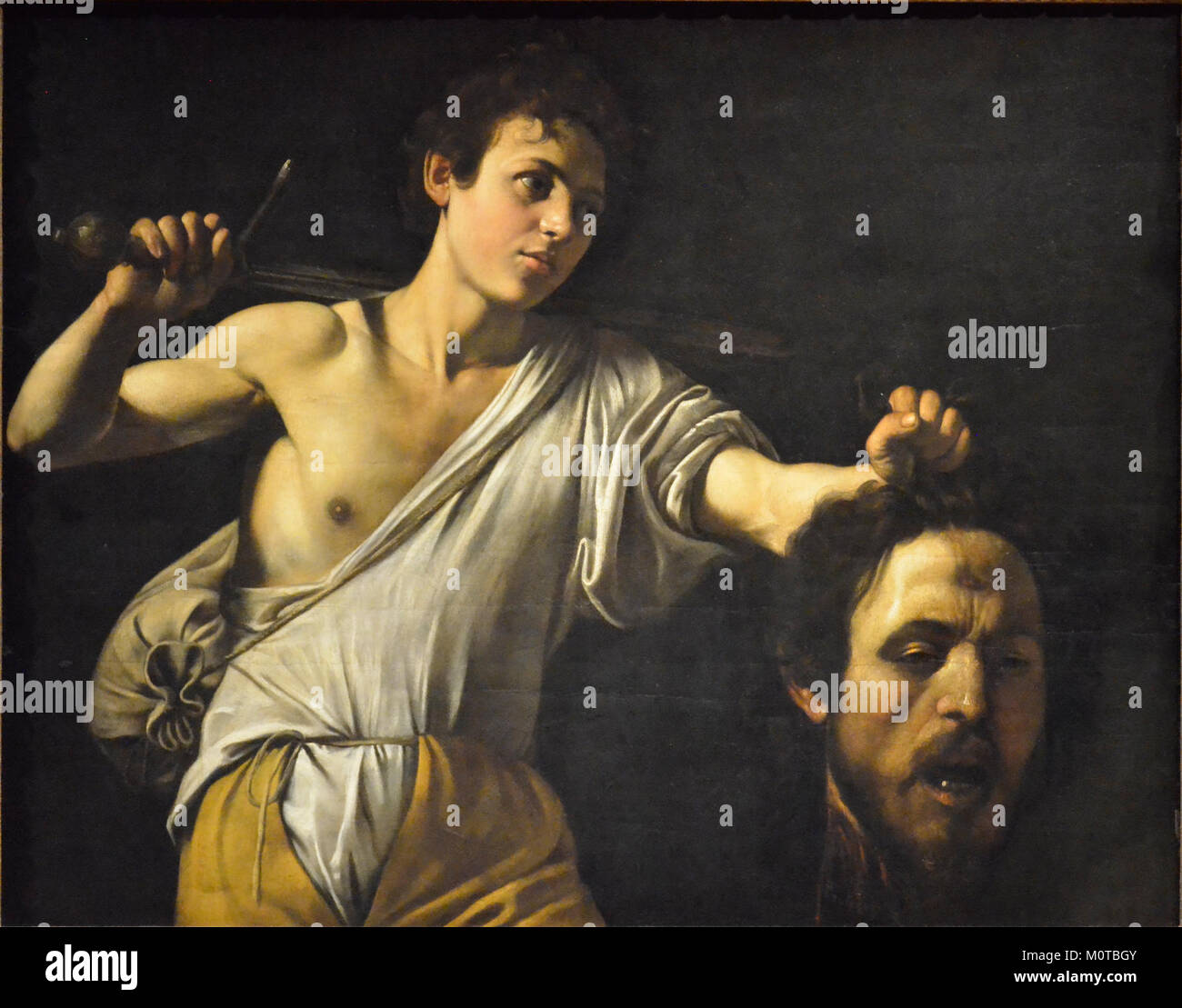 Caravaggios Gemälde *David und Goliath* veranschaulicht die biblische Geschichte von Davids Sieg über Goliath. Das Gemälde ist bekannt für seine dramatische Verwendung von Licht und Schatten, ein Markenzeichen von Caravaggios Stil. Stockfoto