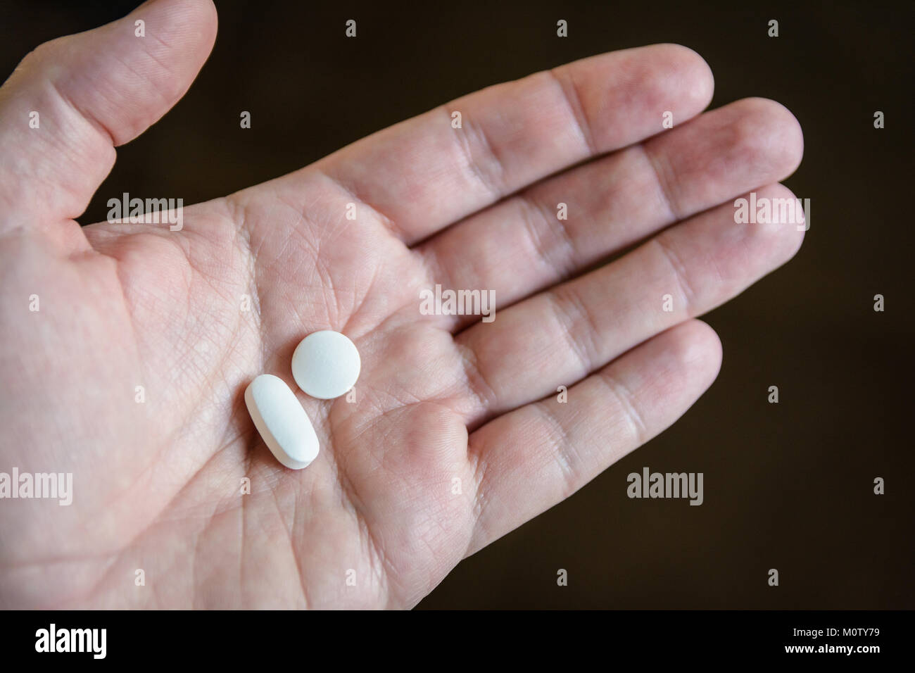 Nahaufnahme von einem weißen männlichen Hand zwei weiße Pillen in der Handfläche vor einem dunklen Hintergrund. Stockfoto