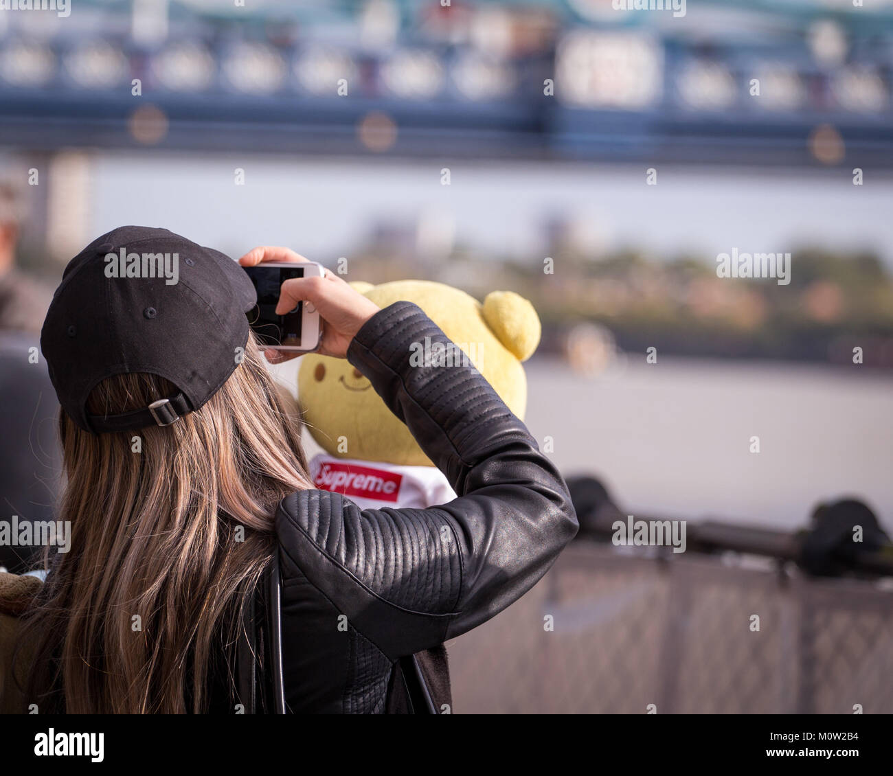 Eine junge Frau ein Bild von ihr Teddy Bär mit der Londoner Tower Bridge im Hintergrund Stockfoto