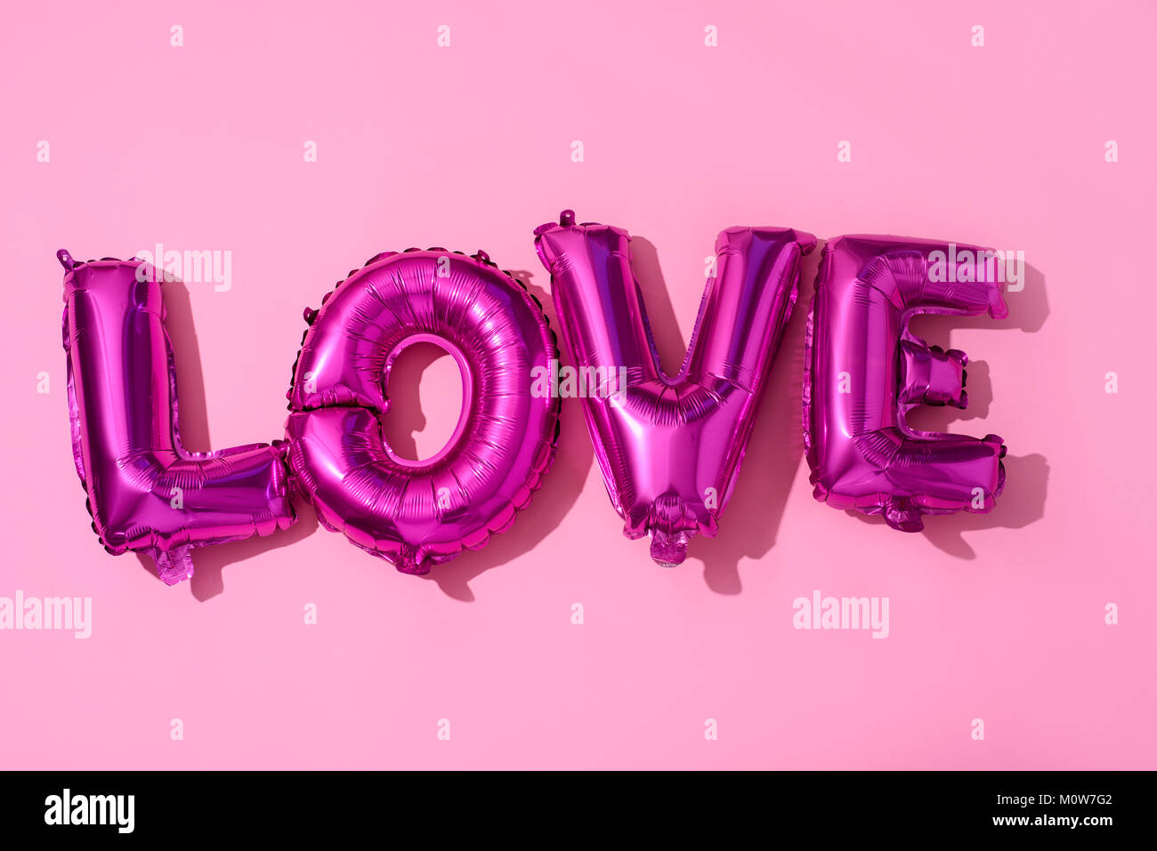 Einige fuchsia Brief-förmige Ballons bilden das Wort Liebe gegen einen rosa Hintergrund Stockfoto