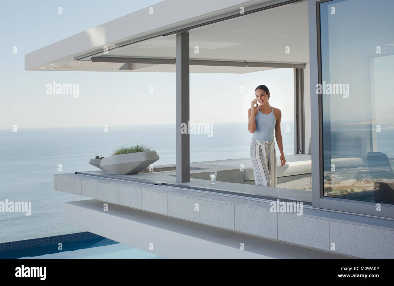 Frau Gespräch am Handy auf moderne, luxuriöse Home Showcase äußere Terrasse mit Meerblick Stockfoto