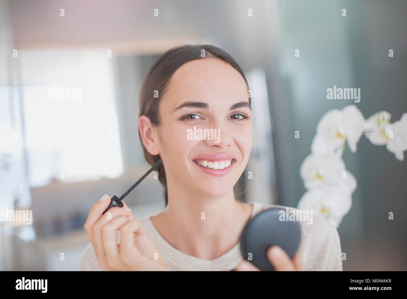 Porträt Lächeln, selbstbewusste Frau mascara Anwendung mit Mascara, Zauberstab und kompakte Spiegel Stockfoto