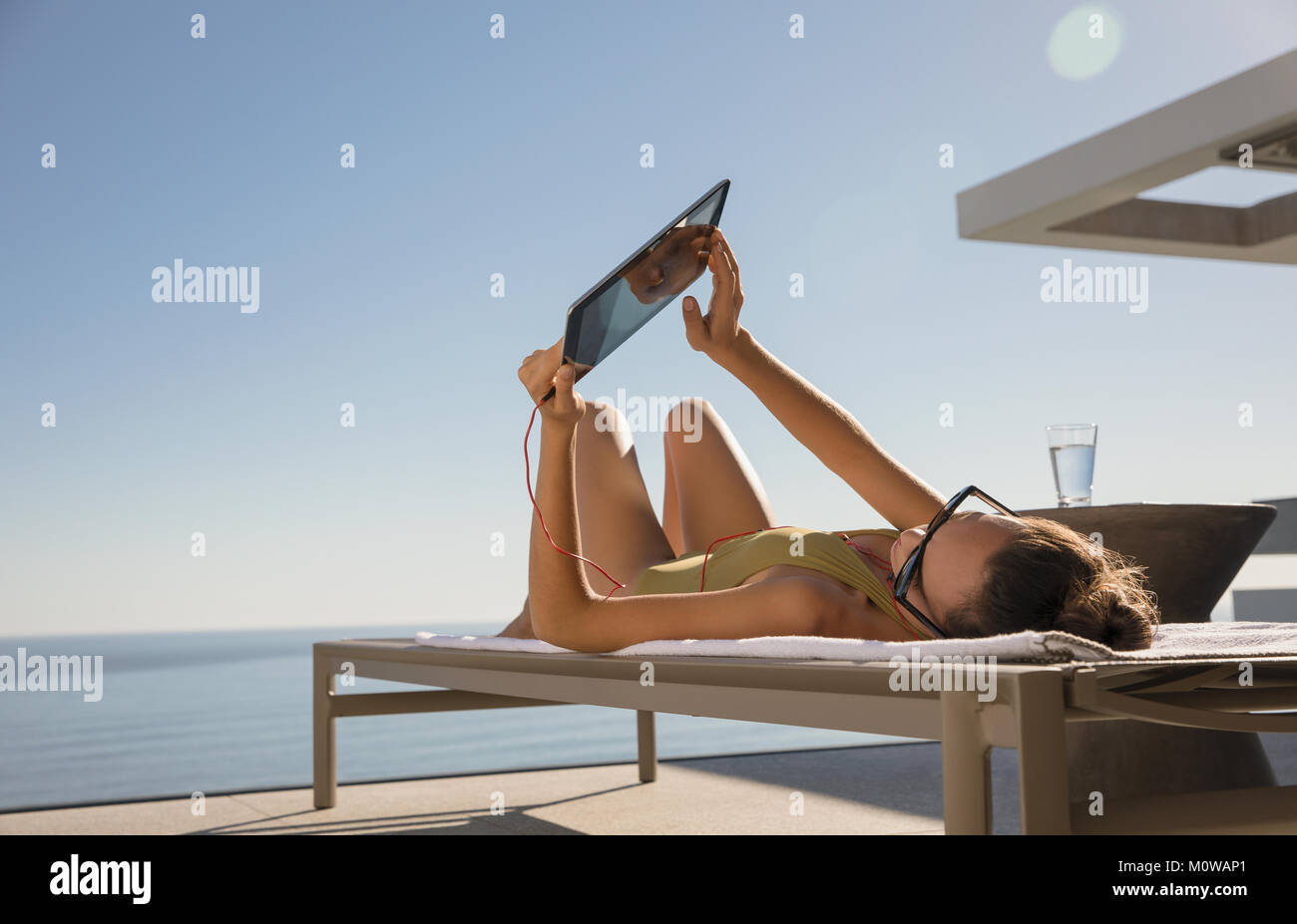 Frau sonnenbaden, mit digitalen Tablette auf Lounge Chair auf der sonnigen Terrasse Stockfoto