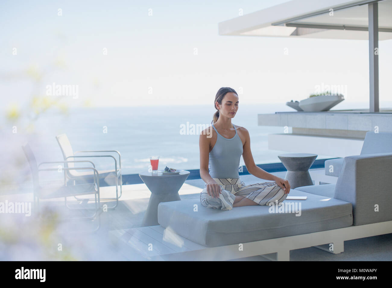 Heitere Frau Meditation im Lotussitz auf moderne, luxuriöse Home Showcase Außenbereich Terrasse Balkon mit Meerblick Stockfoto