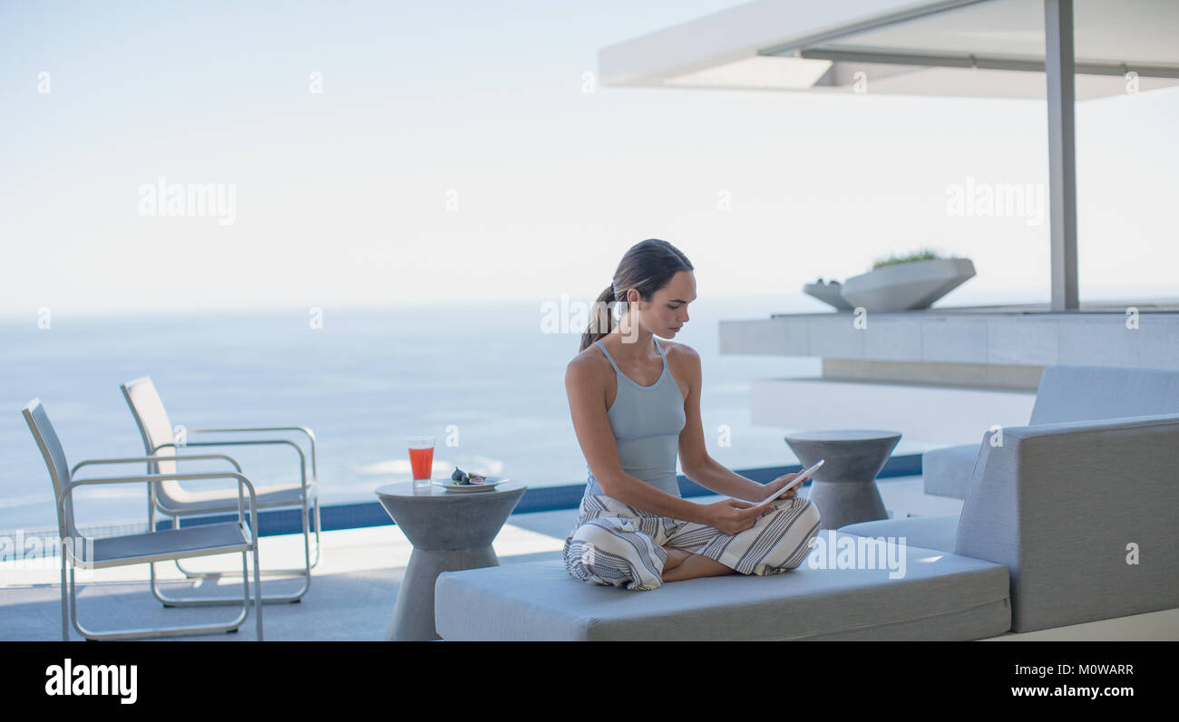 Frau im Schlafanzug mit digitalen Tablette auf moderne, luxuriöse Home Showcase äußere Terrasse mit Meerblick Stockfoto