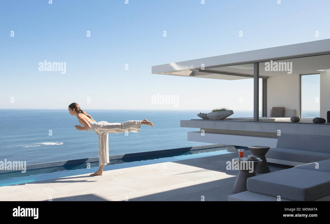Frau yoga Krieger 3 Pose an sonnigen moderne und luxuriöse Home Showcase äußere Terrasse mit Meerblick Stockfoto