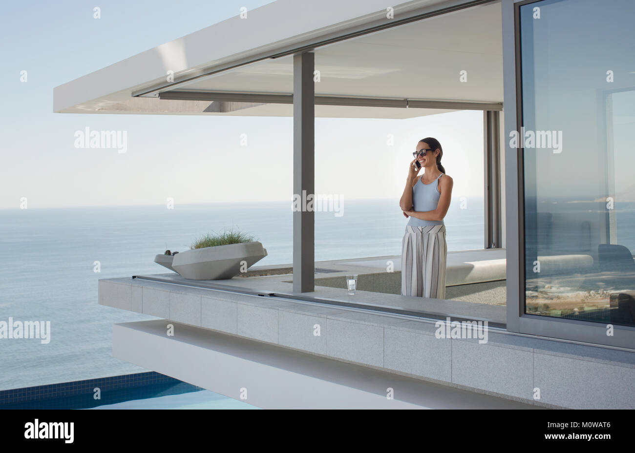 Frau Gespräch am Handy auf moderne, luxuriöse Home Showcase äußere Terrasse mit Meerblick Stockfoto