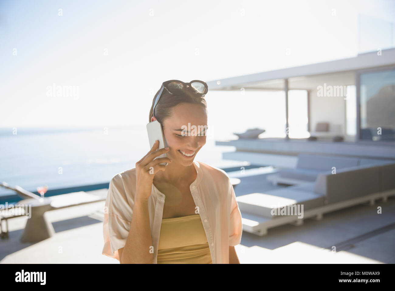 Lächelnde Frau mit Smart Phone an sonnigen moderne und luxuriöse Home Showcase äußere Terrasse Stockfoto