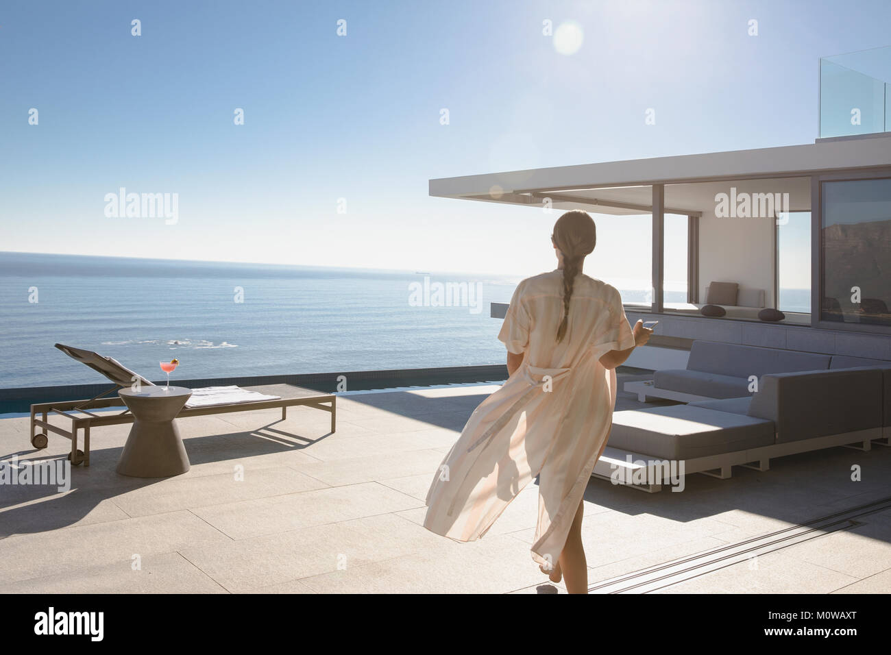 Frau gehen auf sonnige moderne und luxuriöse Home Showcase äußere Terrasse mit Meerblick Stockfoto