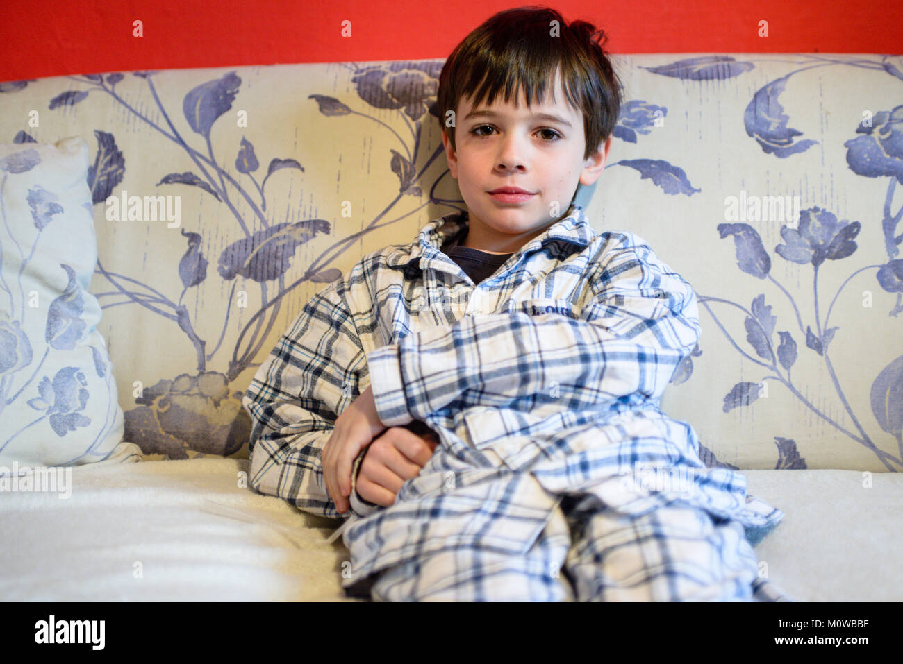 6-jährigen Jungen im Schlafanzug auf dem Sofa sitzen sieht in die Kamera Stockfoto