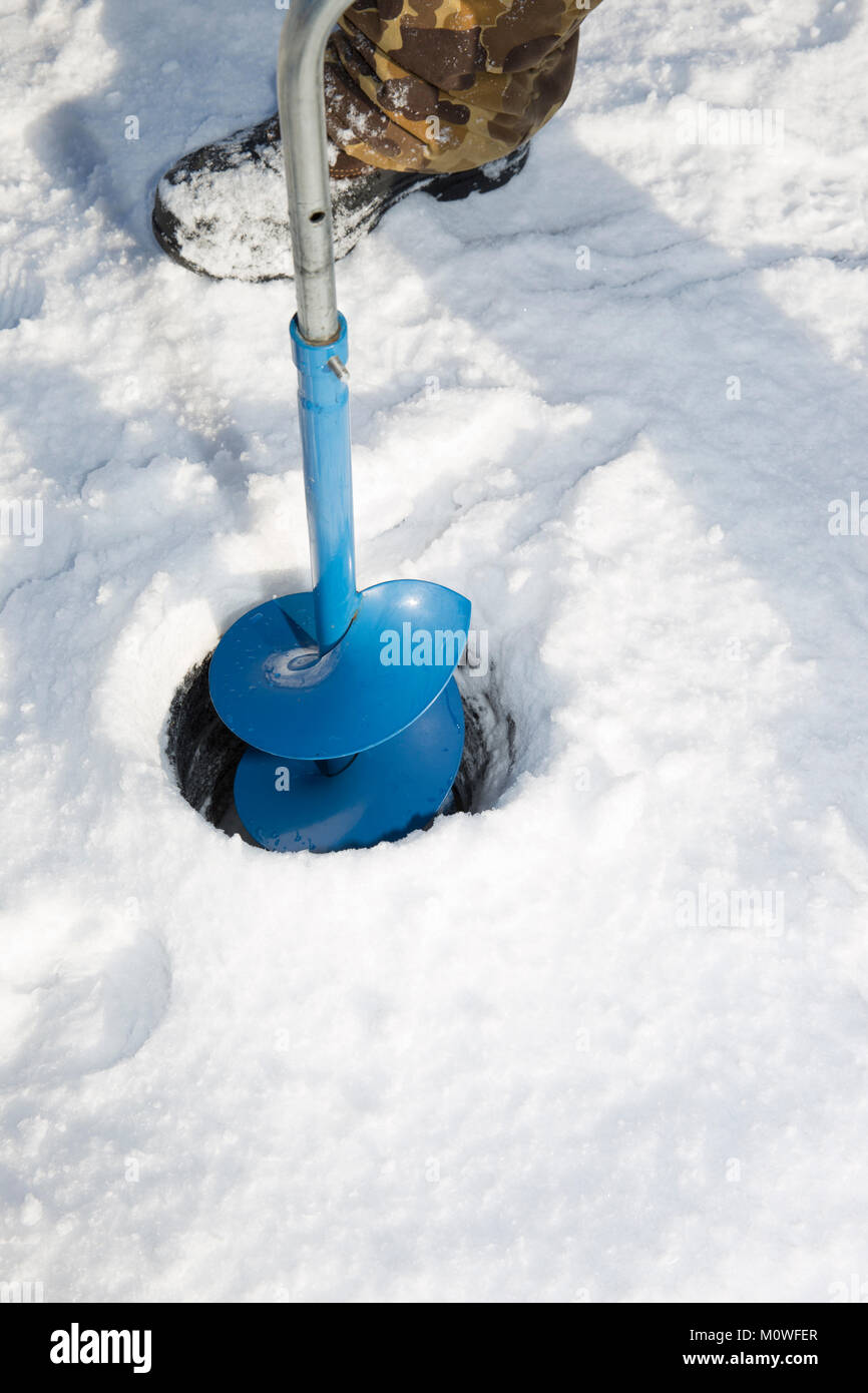 Eine Person bohren ein Loch in das Eis eines zugefrorenen See mit einem Eis auguer (einer spiralförmigen Schraube Blade). Stockfoto