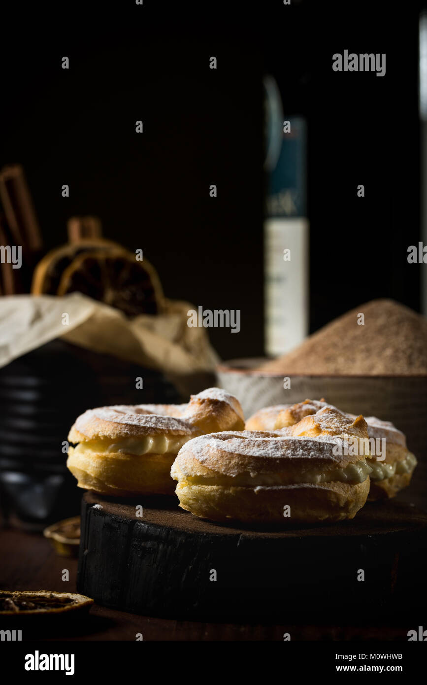 Vertikale Foto von drei hausgemachter Windbeutel. Süße Kuchen mit Sahne gefüllt und dunklem Holz Brett angeordnet mit einer Flasche Rotwein, Zimt Stockfoto