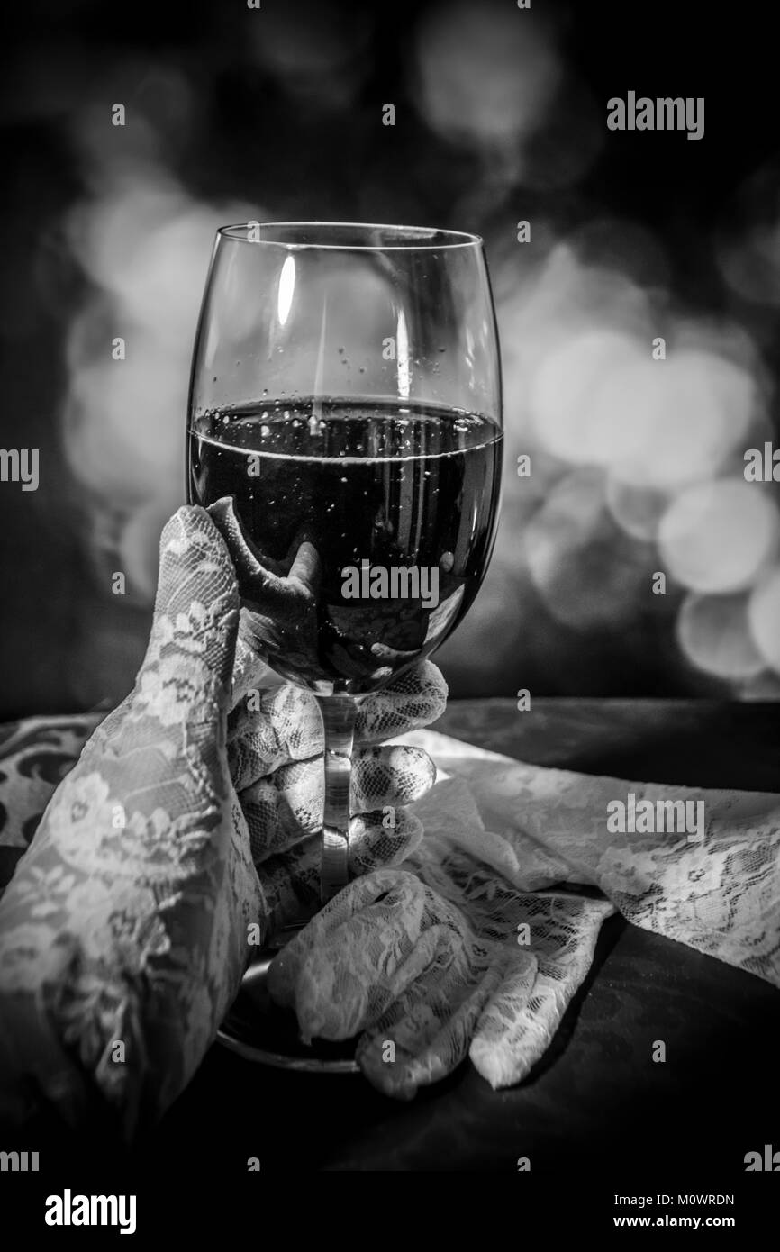 Ein schwarz-weiß Foto von einer Hand in weißen Handschuh hält ein Glas Wein. Stockfoto