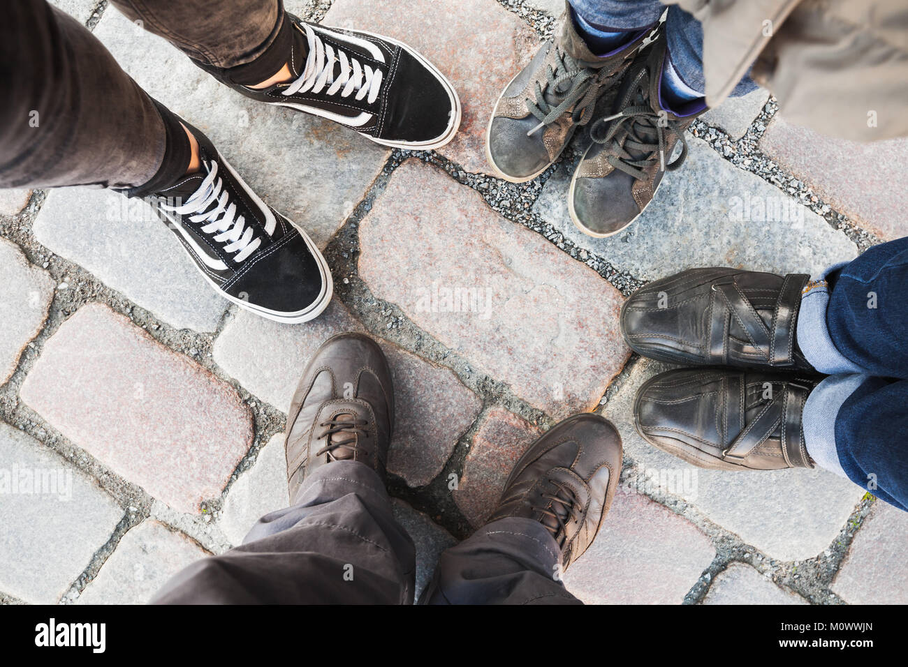 Füße von Mann, Frau, Teenager und Kinder. Echte Familie steht zusammen im Kreis auf gepflasterten Straße. Ansicht von oben Stockfoto