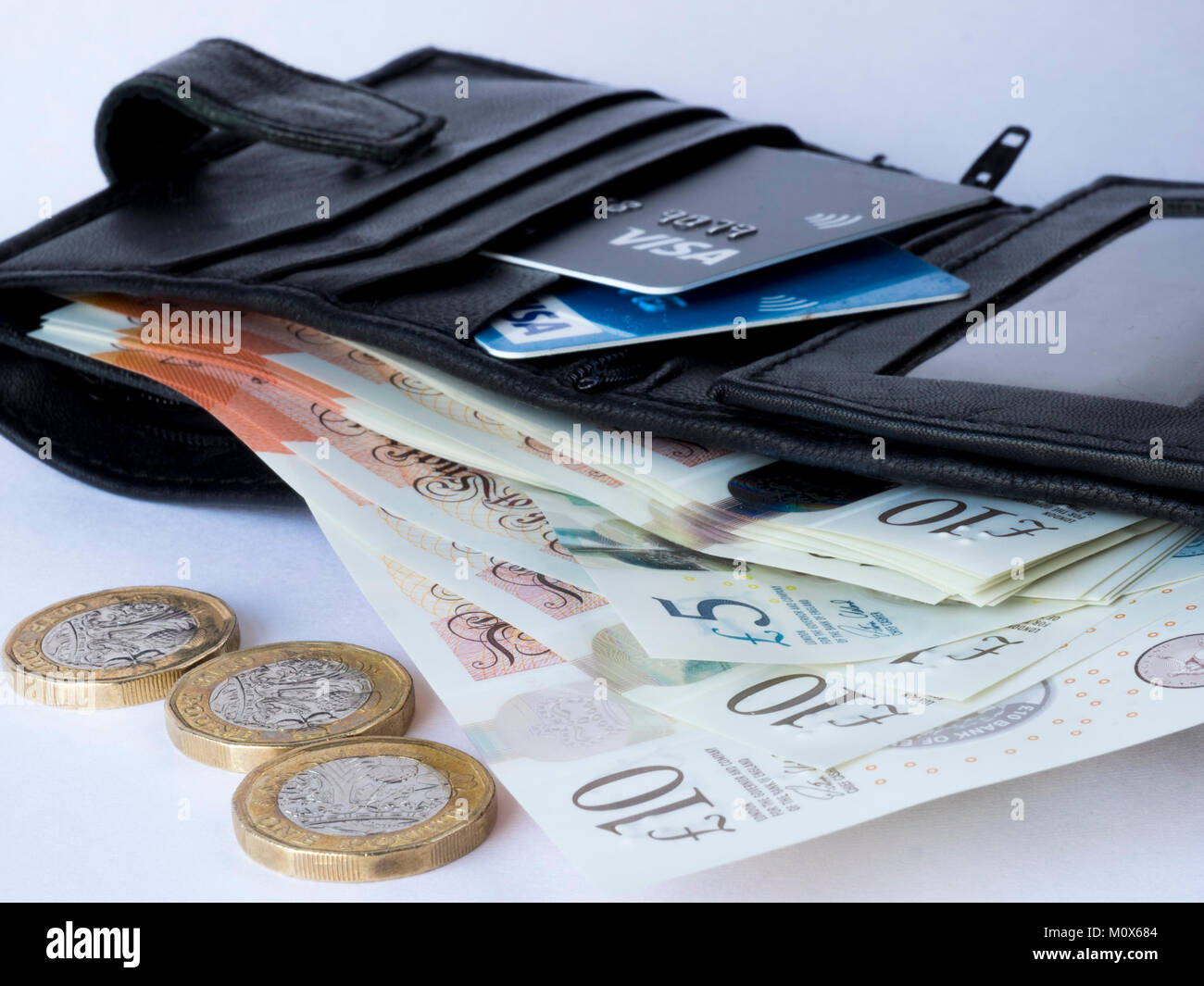 Ein schwarzes Leder Etui mit Kredit- und Debitkarten und Papier Währung mit drei Pfund Münzen im Vordergrund. Stockfoto