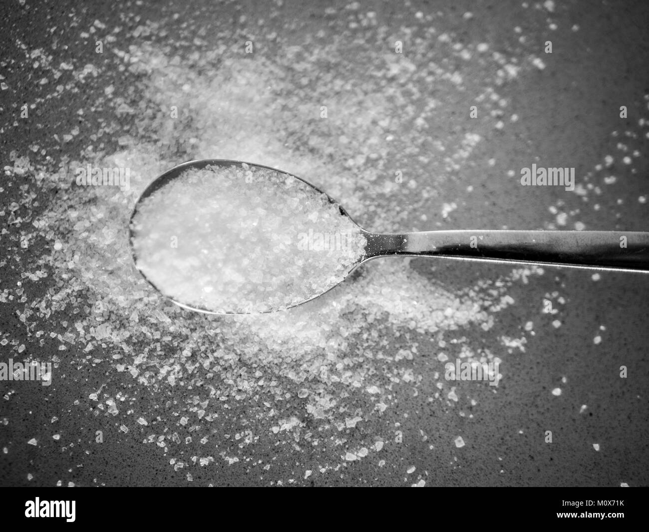 Grobes Salz Körner in verschiedenen Größen in einem Löffel und Verbreitung auf dem Kochen Oberfläche in der Küche Stockfoto