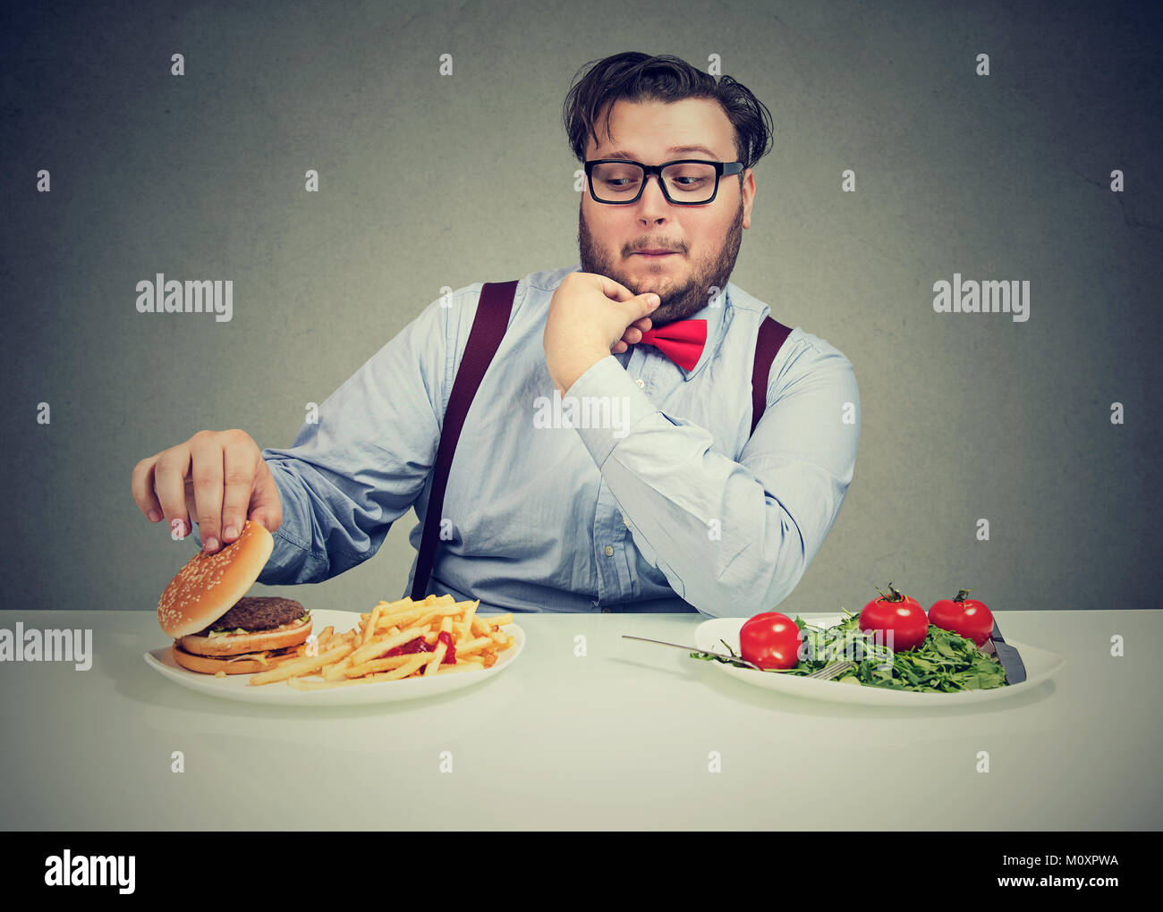 Junge Mann glücklich suchen Bei Burger mit Fleisch anstelle von gesunder Salat. Stockfoto